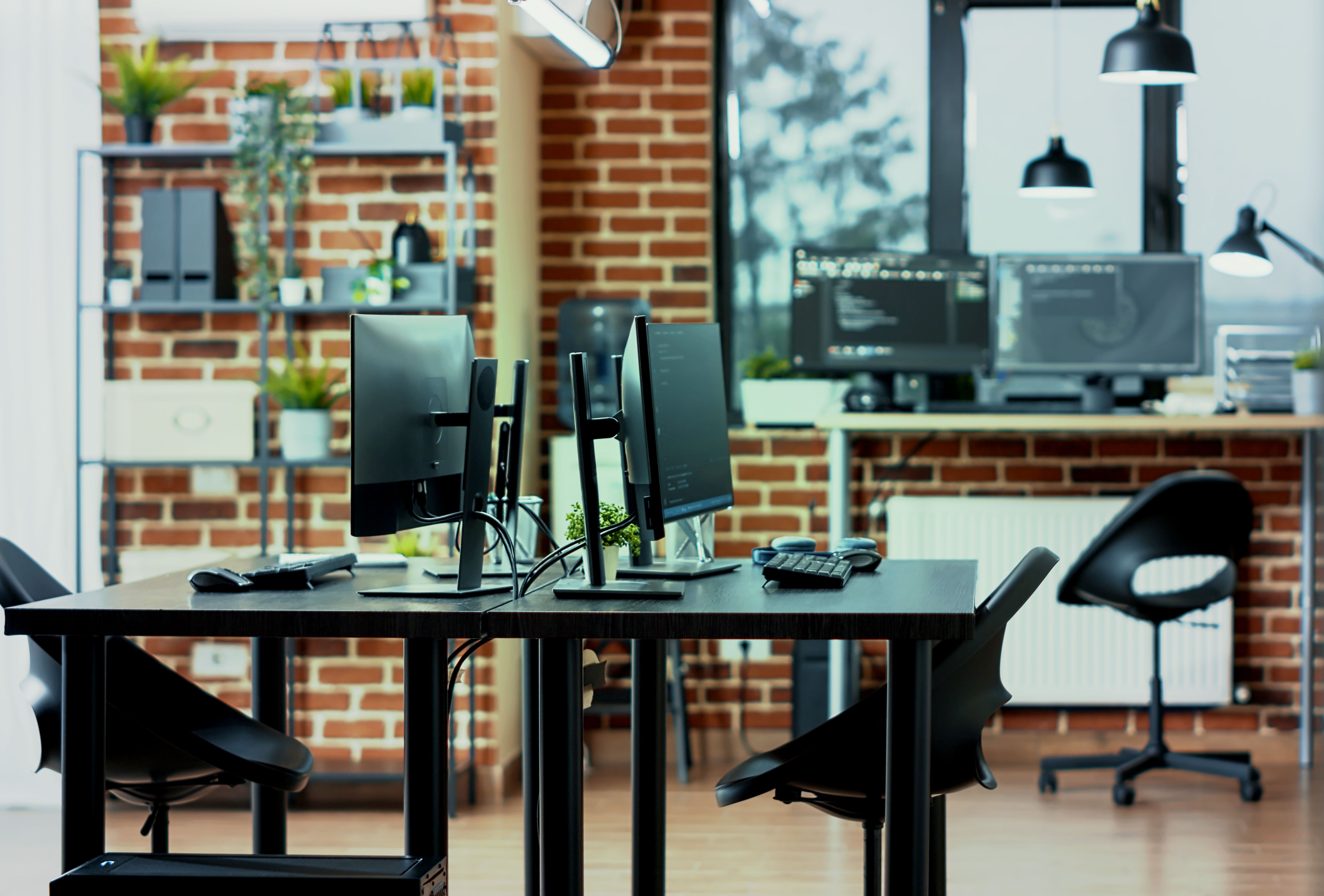 Close-up of computer screens on a desk in a tech workspace, displaying programming code, data algorithms, and cloud computing software, with a background of servers and neural network visuals.
